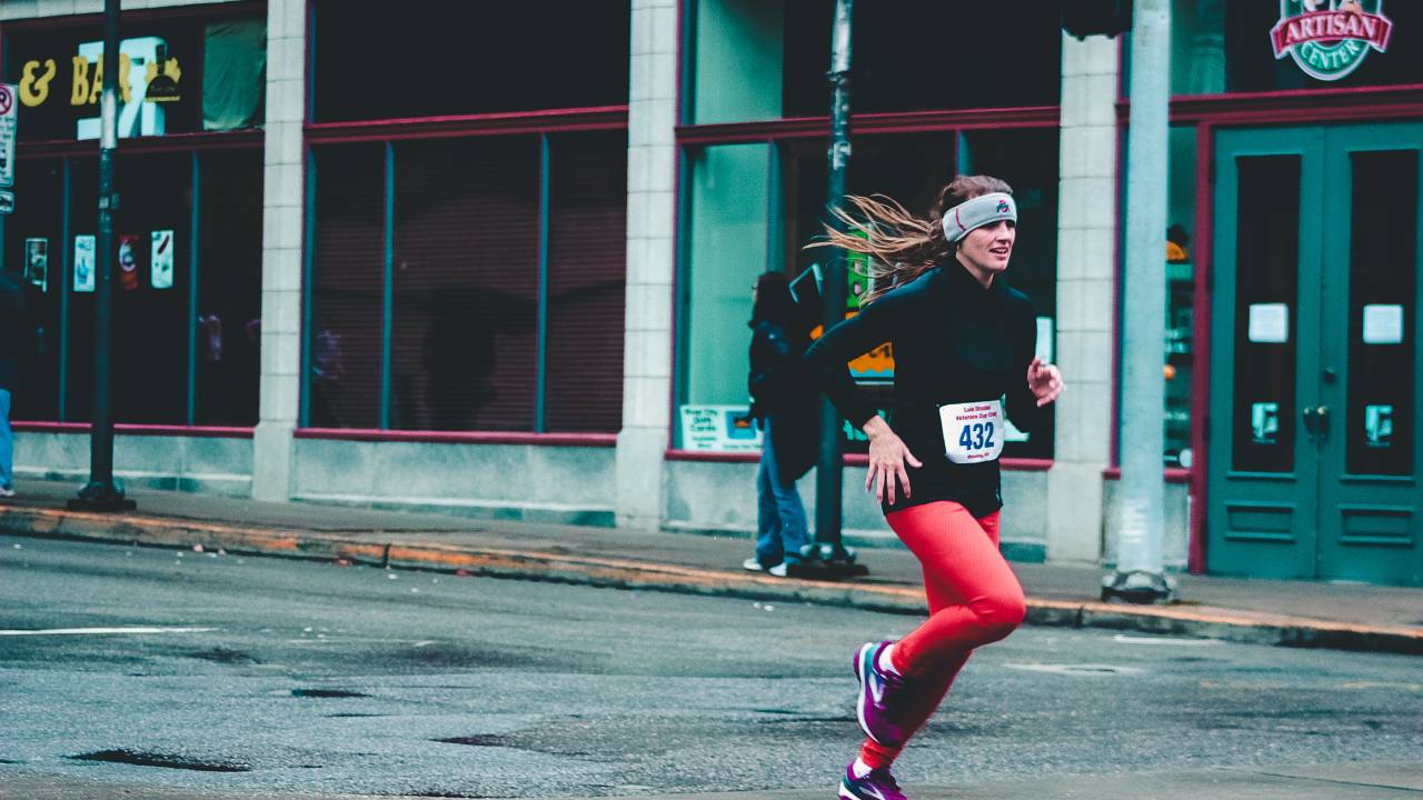 Uma mulher está correndo uma maratona em uma rua vazia, apenas com uma pessoa na calçada