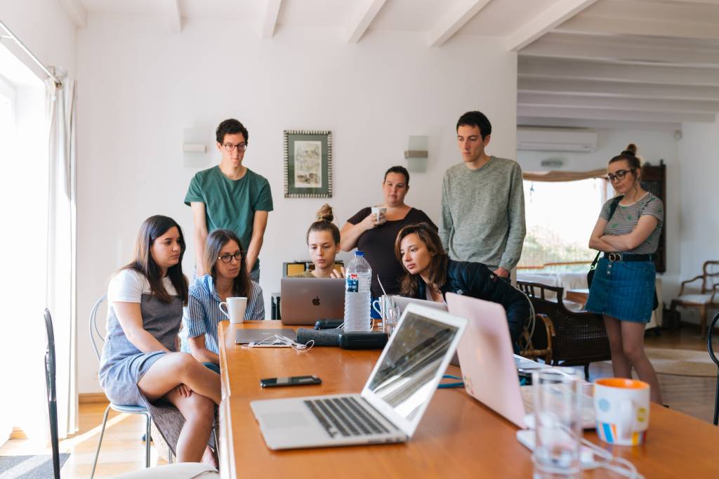 Um grupo de oito pessoas estão olhando para um computador. Quatro delas estão sentadas, as outras estão atrás, de pé