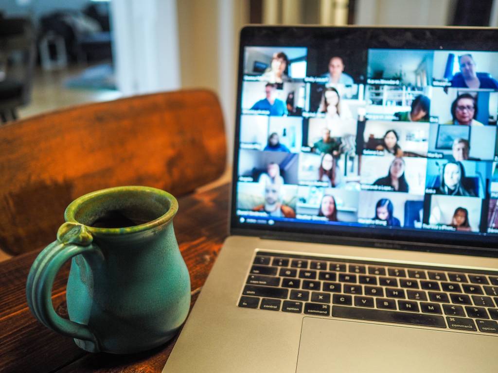Imagem mostra notebook com a tela mostrando várias pessoas em uma reunião online. Ao lado, uma caneca de cerâmica cor turquesa