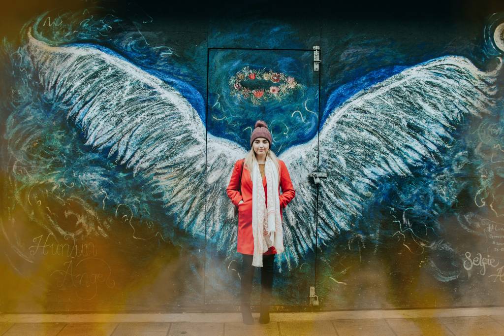 Mulher está em frente a uma parede com pintura de asas de anjo