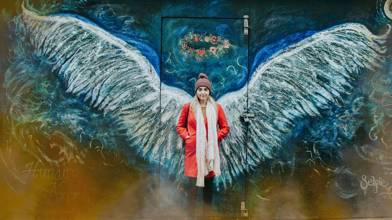 Mulher está em frente a uma parede com pintura de asas de anjo
