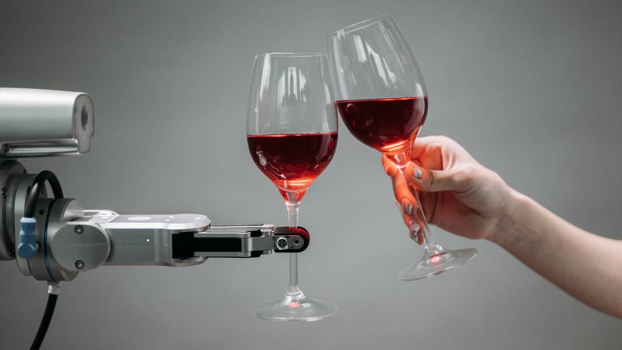 Um robô segura uma taça de vinho e faz um brinde com um ser humano, que segura uma segunda taça.