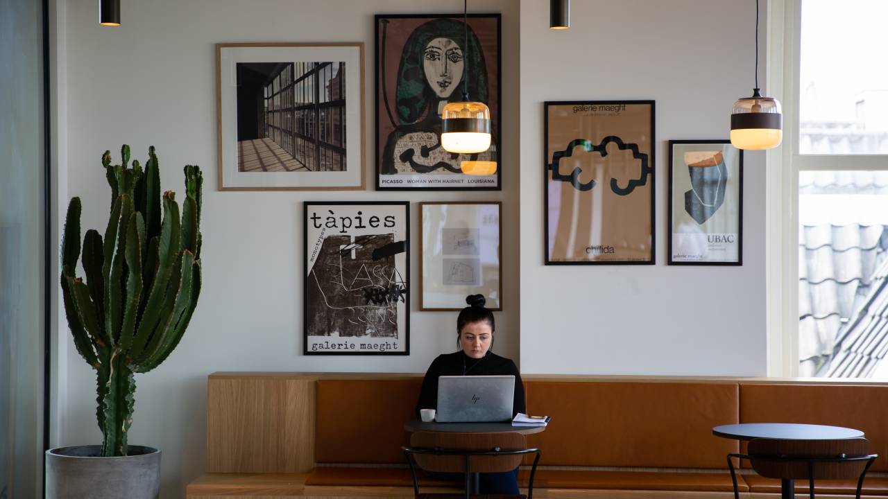 Mulher trabalha em um espaço compartilhado em frente a uma gallery wall