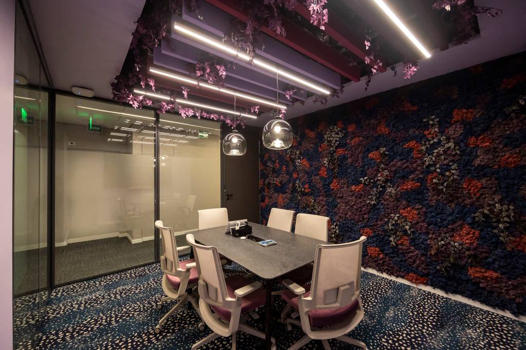 Sala de reunião com carpete estampado, mesa com seis cadeiras e lustre
