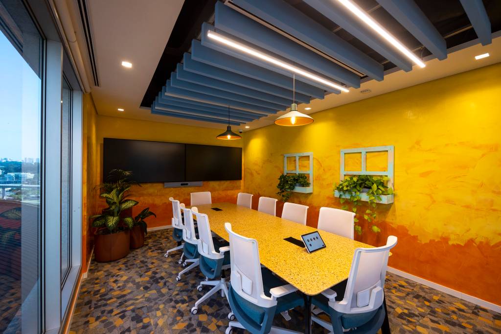 Disney Luca Sala de reuniões com uma mesa de oito cadeiras. Na parede, há duas janelas com jardineiras cenográficas