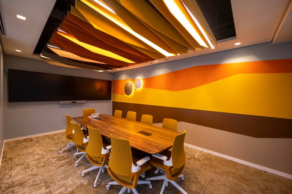 Sala de reunião com uma mesa de oito cadeiras, carpete marrom e parede com ilustração de sol