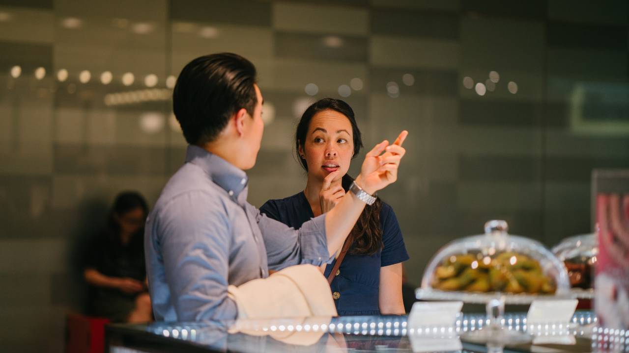 Um homem e uma mulher asiáticos conversam em um balcão de cafeteria