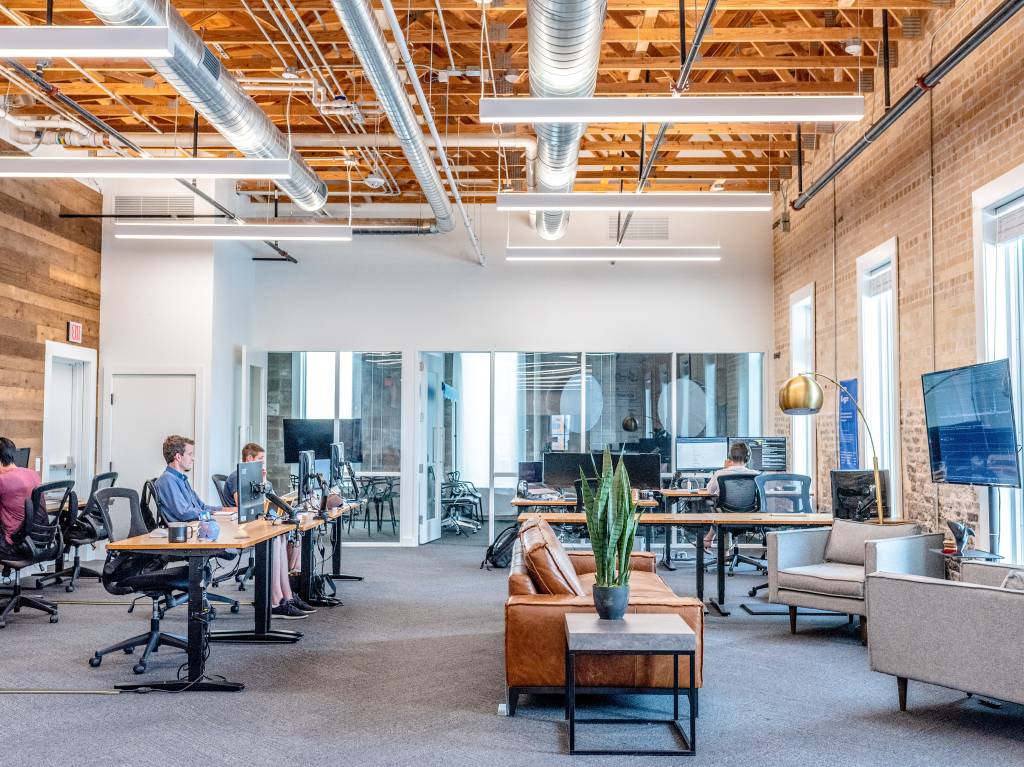 A imagem mostra um escritório moderno com algumas pessoas trabalhando