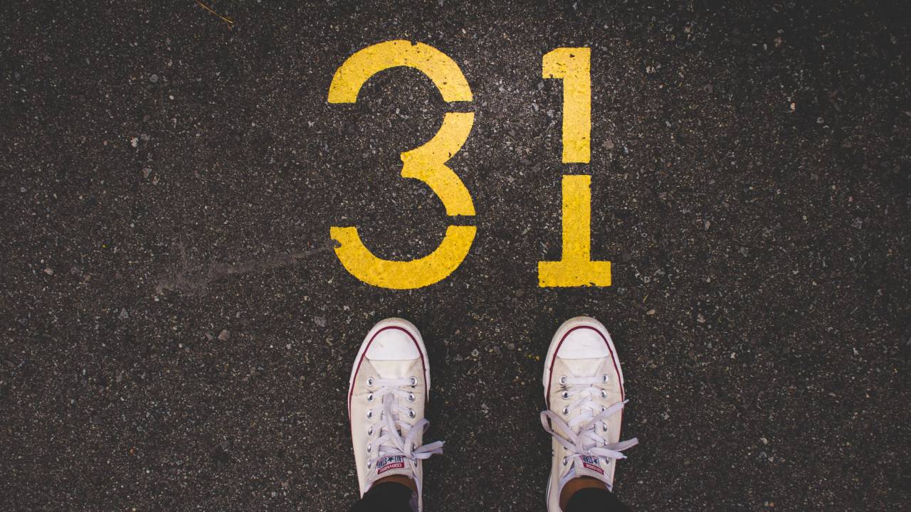 Imagem mostra uma pessoa em pé sobre o asfalto, com all star branco. No asfalto está pintado o número 31