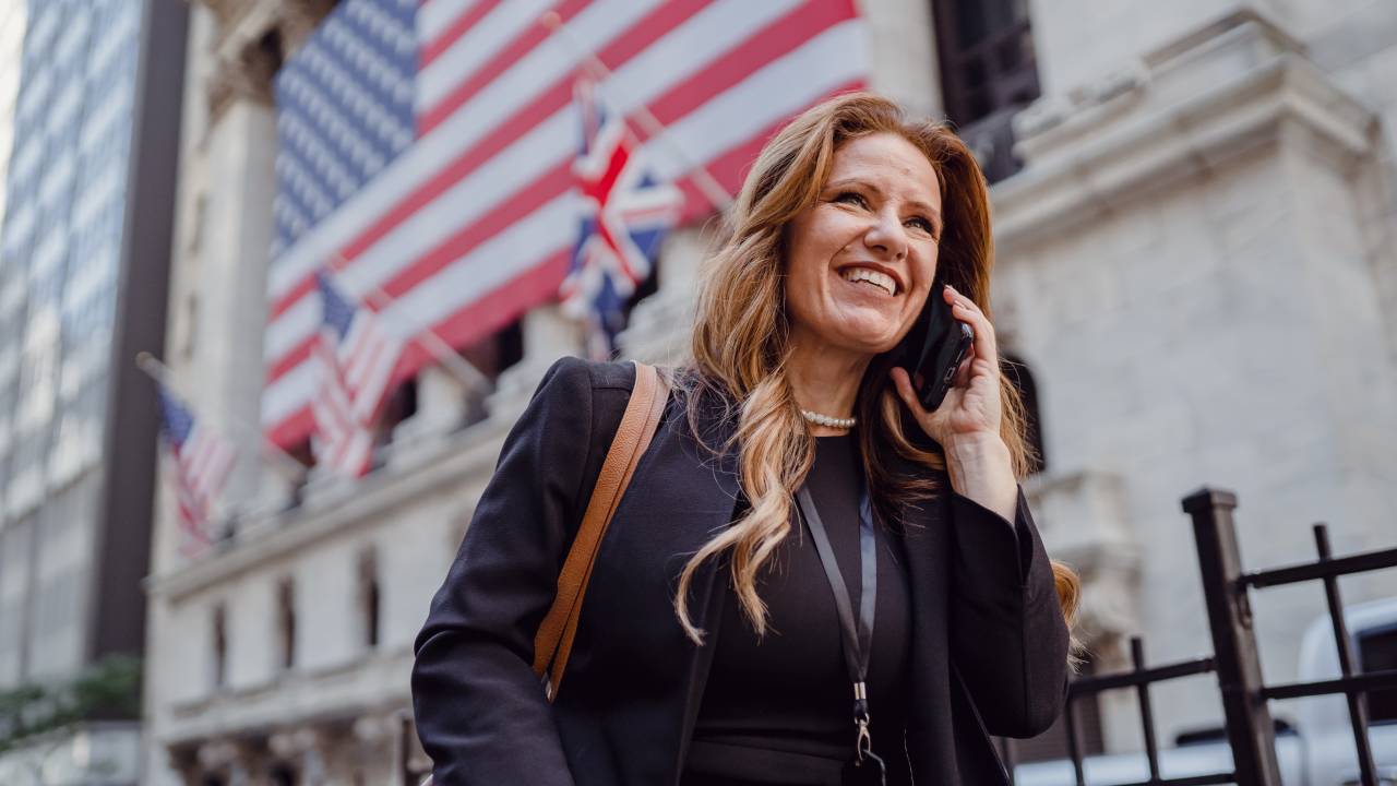 Executiva fala ao celular em frente a um prédio com a bandeira dos Estados Unidos