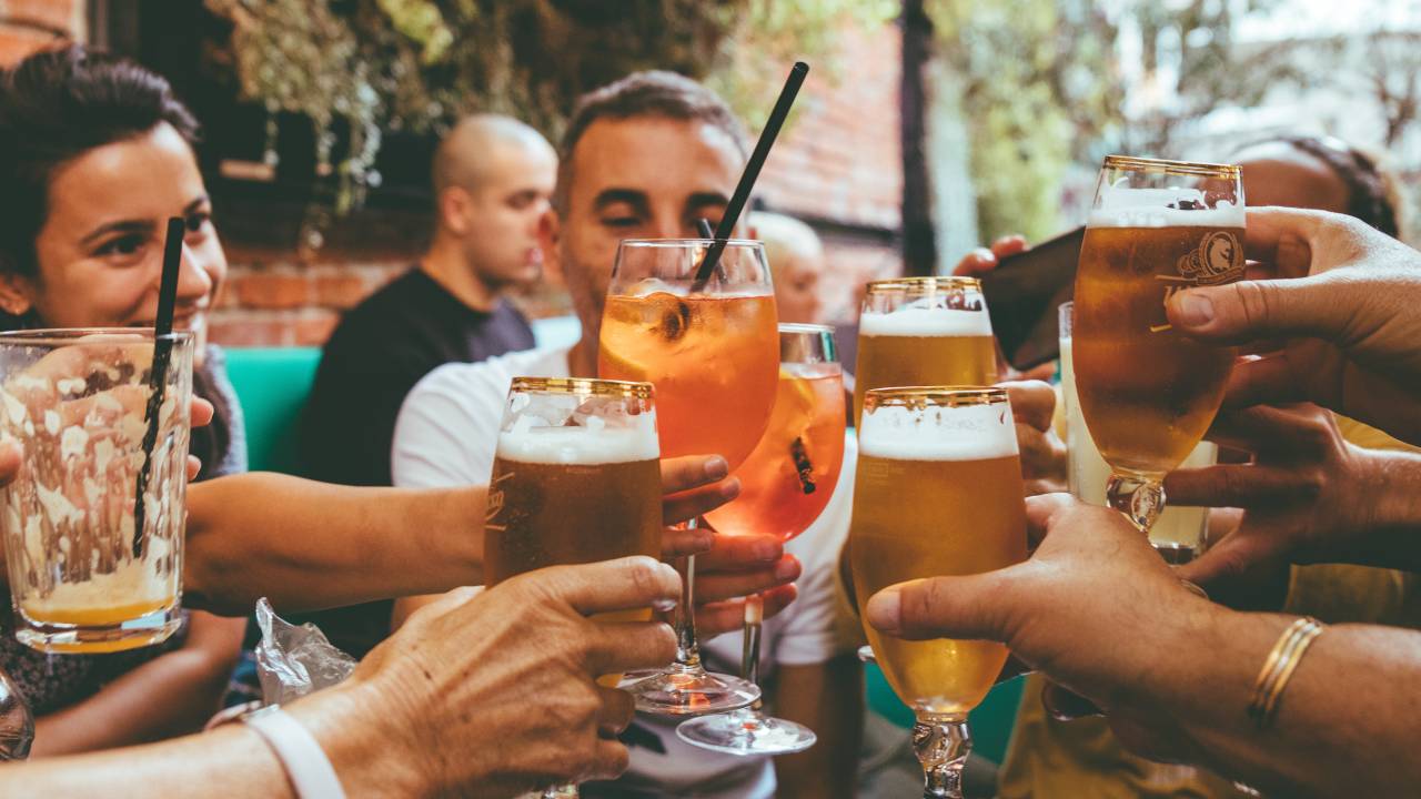 Grupo de pessoas brinda com copos de cerveja e coquetéis em um restaurante com parede de tijolinhos