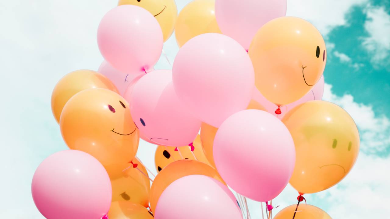 Imagem mostra balões de festa cor-de-rosa e amarelos em formato de emojis alegres e tristes