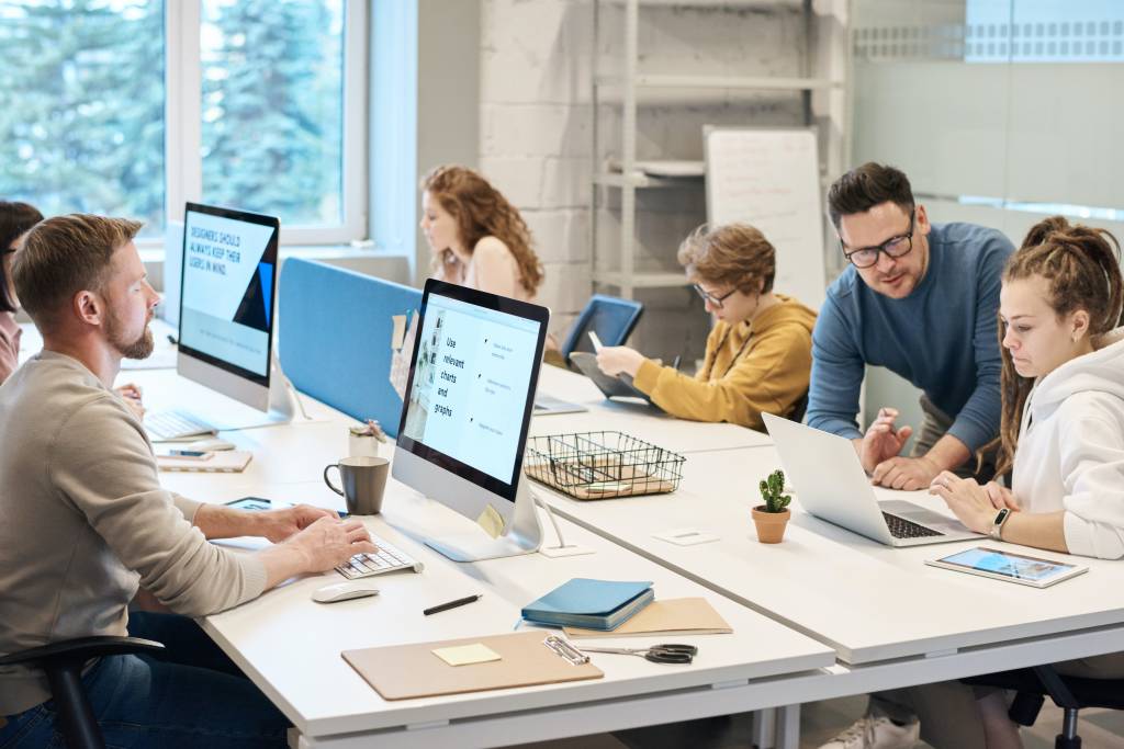 Profissionais trabalham em um escritório com mesões brancos e computadores