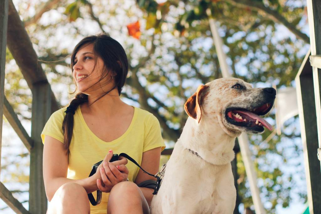 Mulher de camiseta amarela está sentada segurando a coleira de seu cachorro