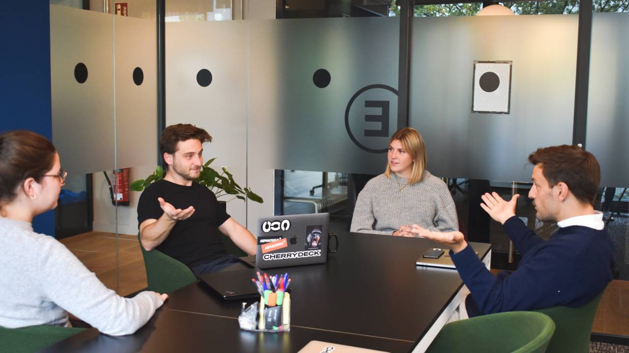 Grupo de quatro pessoas conversa em uma sala de reuniões em uma empresa