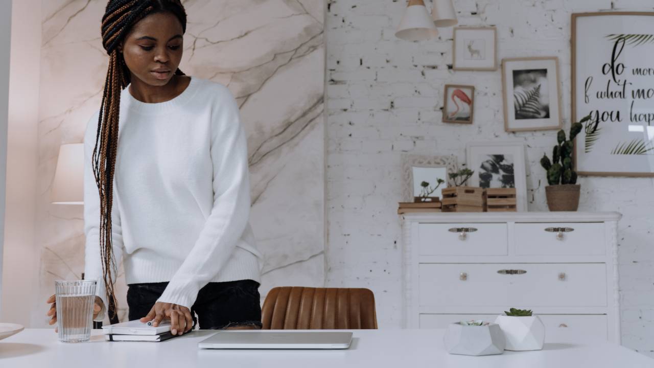Mulher negra em home office olha para a mesa com seu notebook
