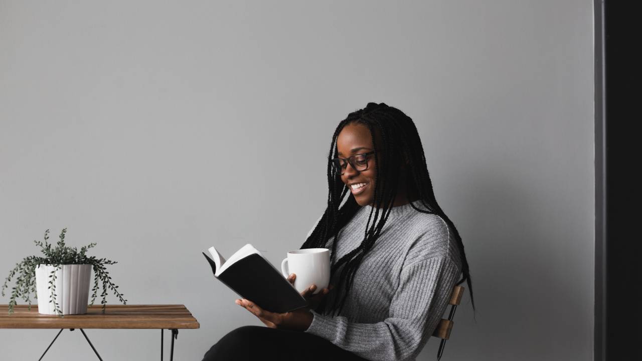 Mulher lê um livro e segura uma xícara de chá