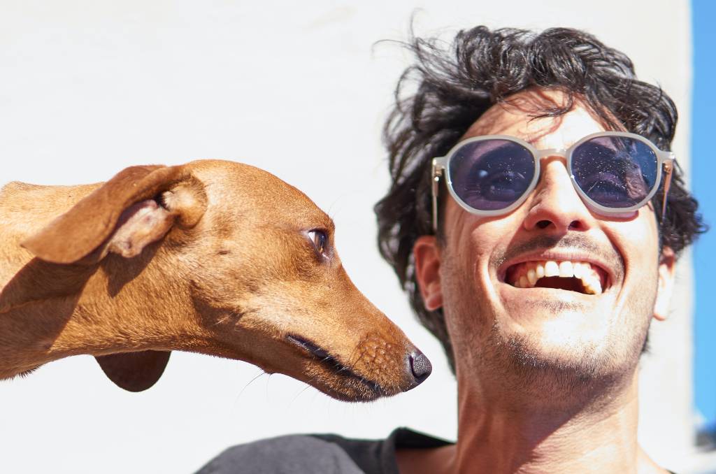Homem de óculos escuros está sorrindo ao lado de um cachorro caramelo