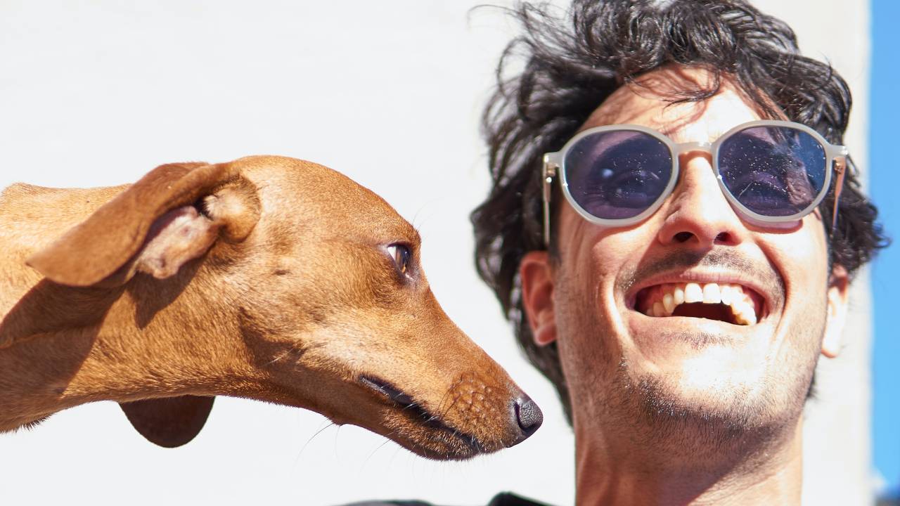 Homem de óculos escuros está sorrindo ao lado de um cachorro caramelo