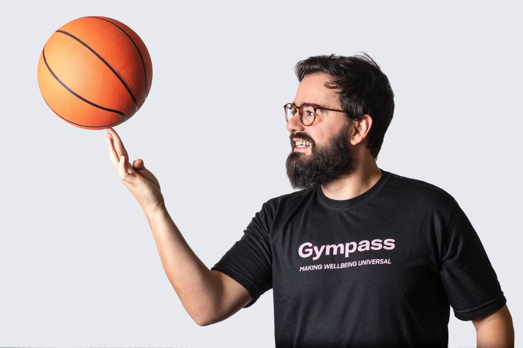 Renato veste uma camiseta preta com o logo do Gympass enquanto gira uma bola de basquete no dedo