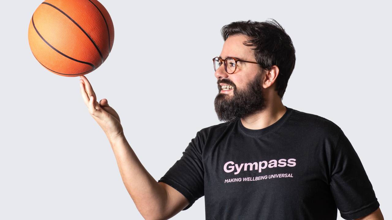Renato veste uma camiseta preta com o logo do Gympass enquanto gira uma bola de basquete no dedo