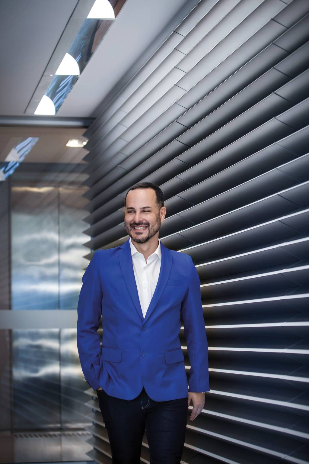 André usa um blazer azul e uma camisa branca enquanto sorri para a foto