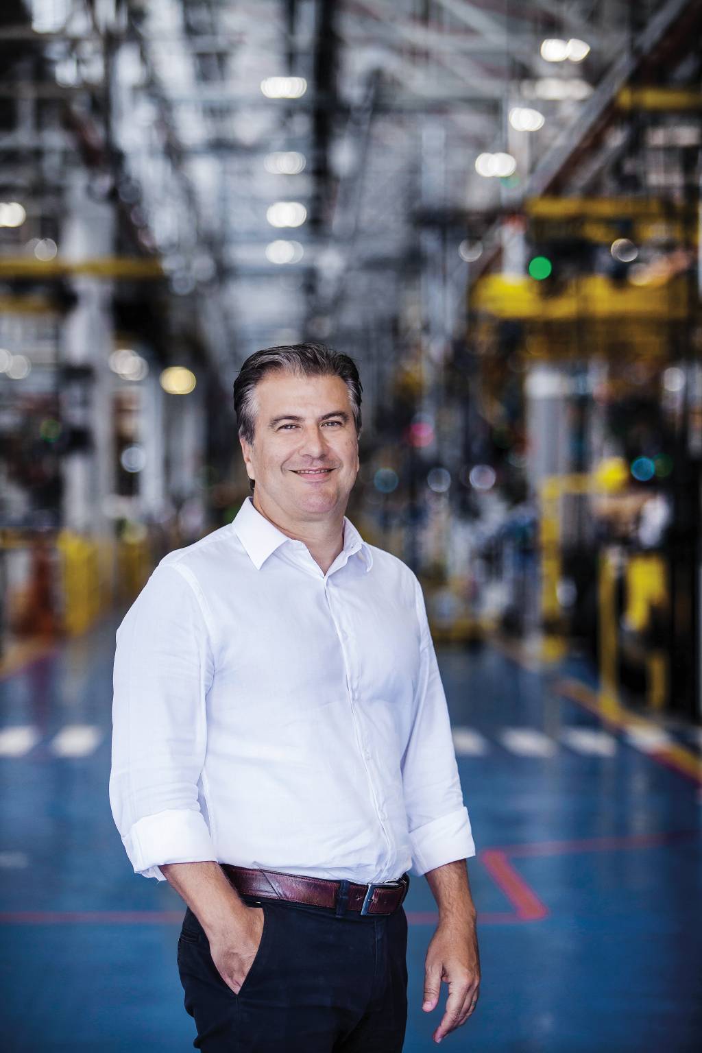 Danilo está em uma fabrica, vestido com calça e camisa social, posando para a foto