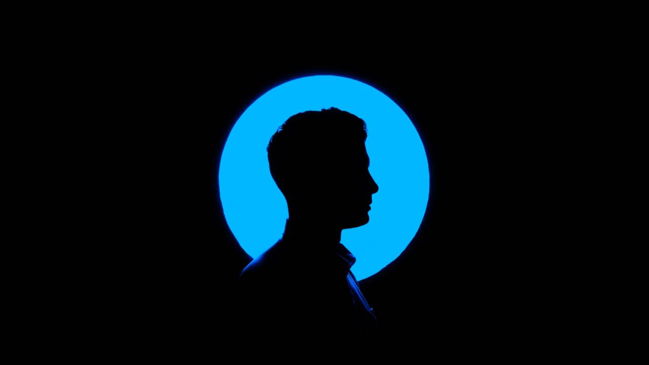 Fundo preto com um circulo iluminado azul. No meio do circulo tem a sombra do perfil de uma pessoa