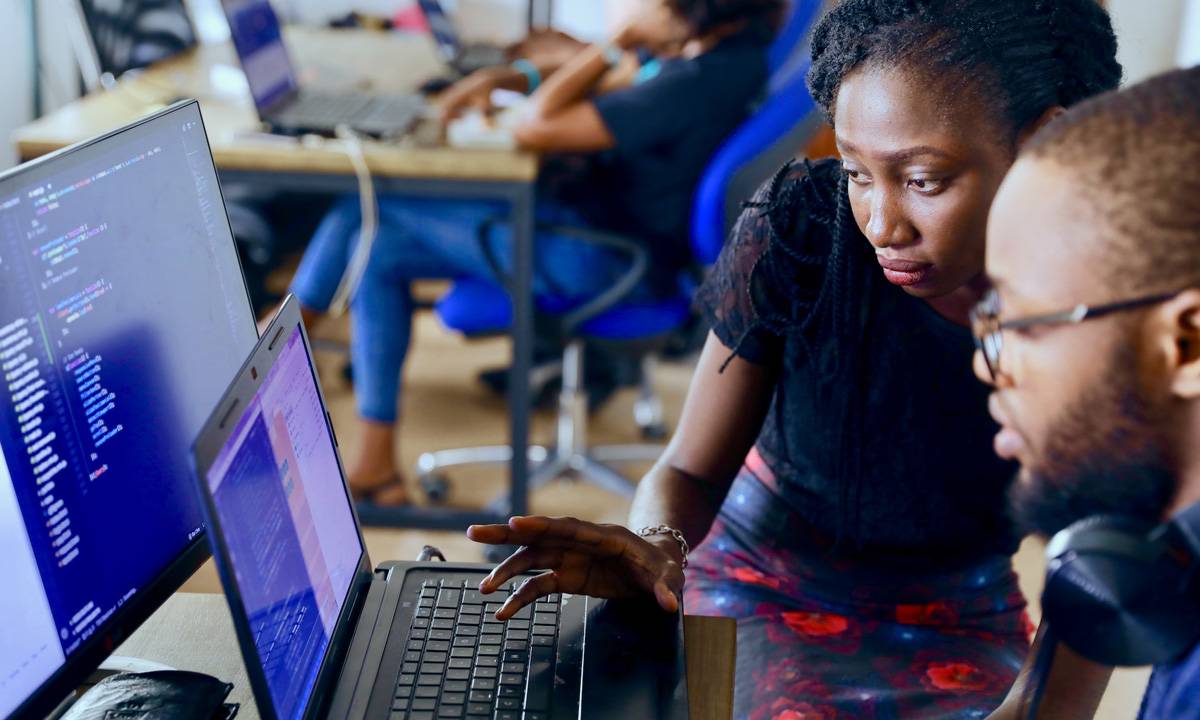 fotografia de uma mulher negra e um homem negro em frente a um computador trabalhando com códigos de programação