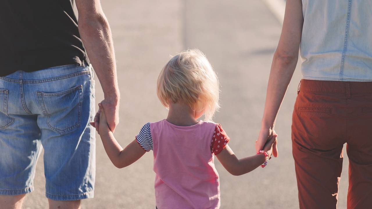 Um homem e uma mulher andam de mãos dadas a uma criança. A foto mostra os três de costas sob o sol