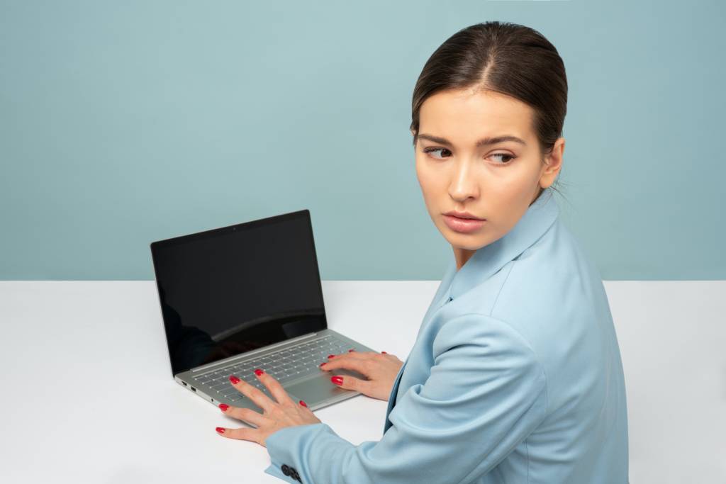 Uma mulher está trabalhando, com as mãos sobre o teclado de seu notebook, enquanto olha para trás, assustada