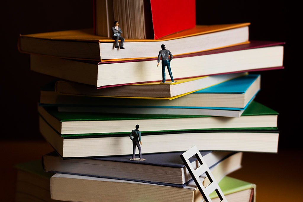 Miniatura de homens vestindo roupas formais escalando pilha de livros.