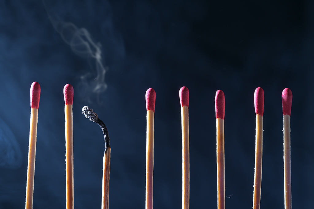 Foto de fileira de fósforos frescos com cabeças vermelhas, um queimou e mostra somente algum fumo, conceito da sobrecarga.