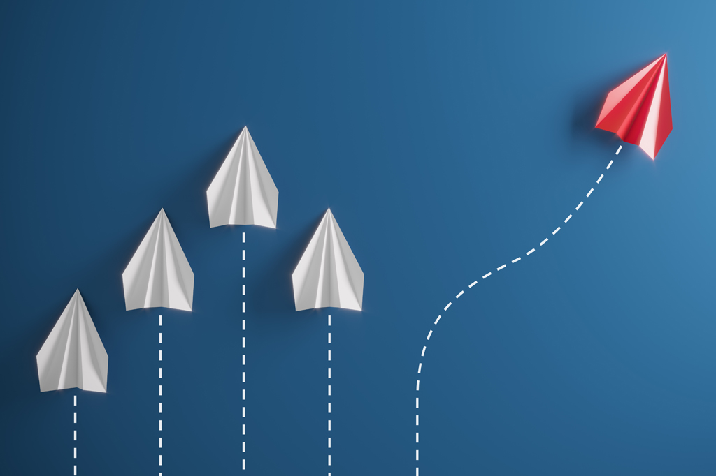 Imagem, em fundo azul escuro, de um grupo de aviões de papel em uma direção e com um indivíduo apontando em direção diferente.