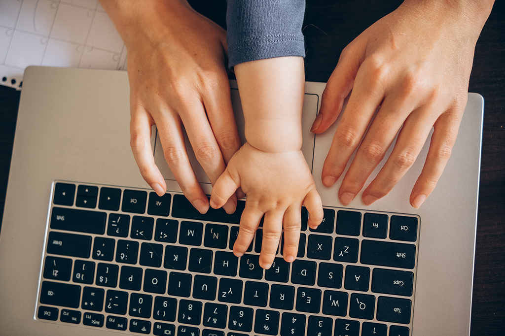 Fotografia de uma mãe e seu bebê com as mãos em um laptop trabalhando.