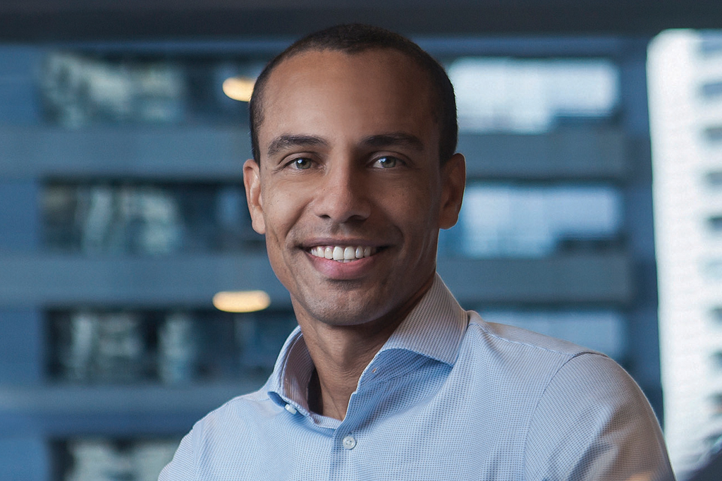 Imagem de um homem sorrindo, de cabelos curtos e vestindo uma camisa azul clara.