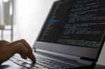 Um homem digitando códigos de programação em um notebook preto