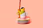 Café sendo derramado em xícaras coloridas empilhadas.