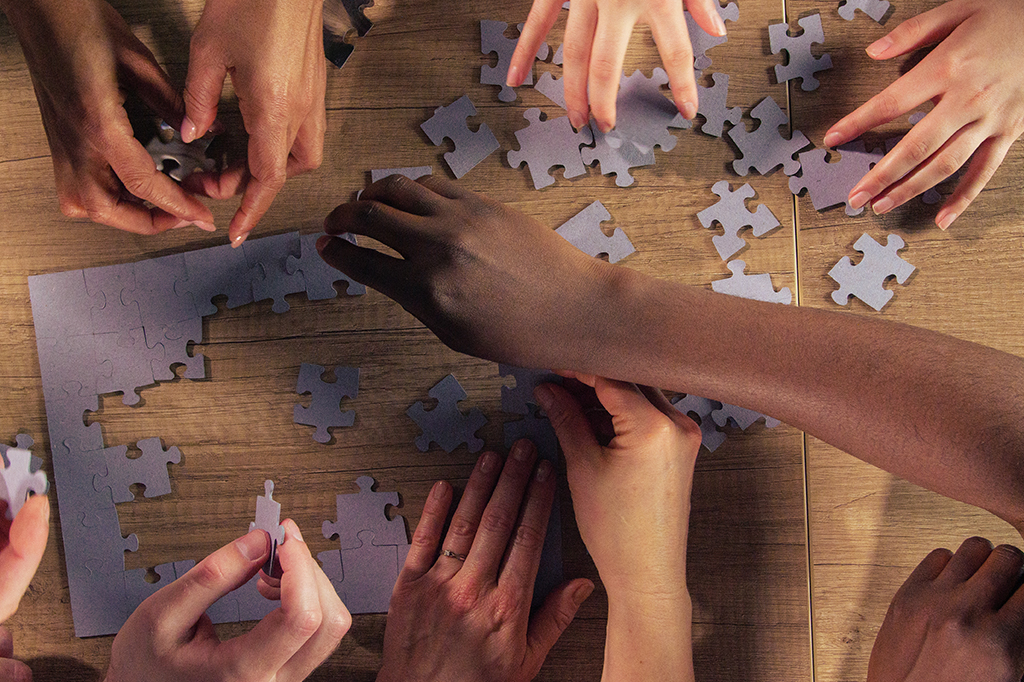 Visão aérea de mãos sobre uma mesa montando um quebra cabeça.