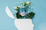 Recorte de papel da silhueta de uma pessoa de perfil. No topo da cabeça, há um pequeno arranjo de flores.