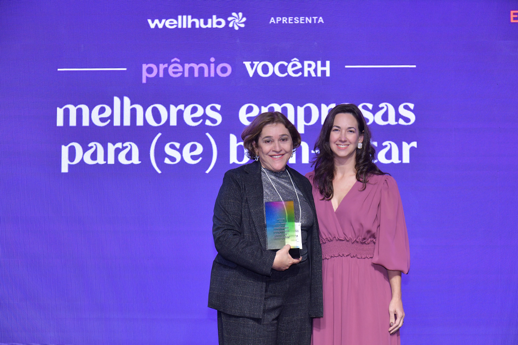 Duas mulheres lado a lado segurando um troféu com as mãos.