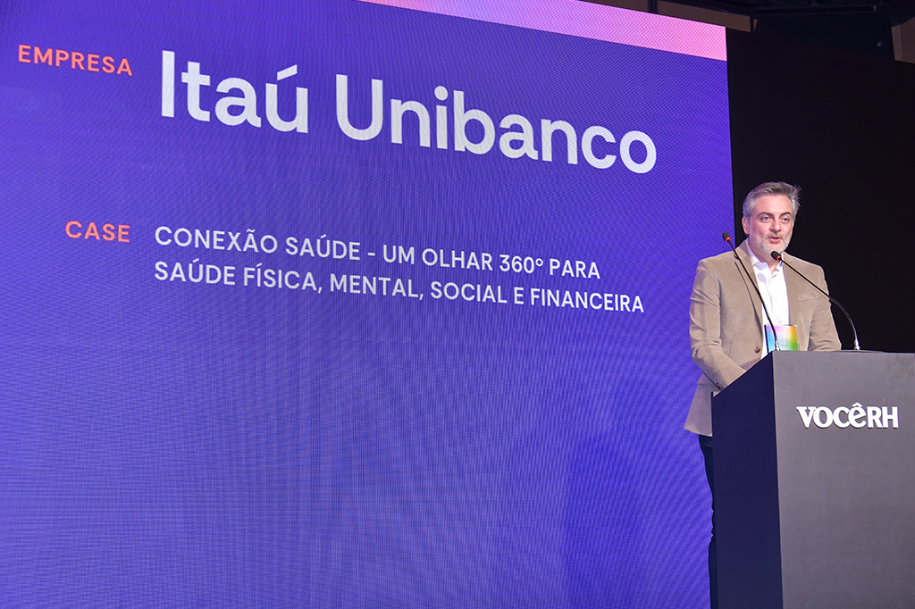 Um homem em cima de um palco diante de um púlpito, falando em um microfone.