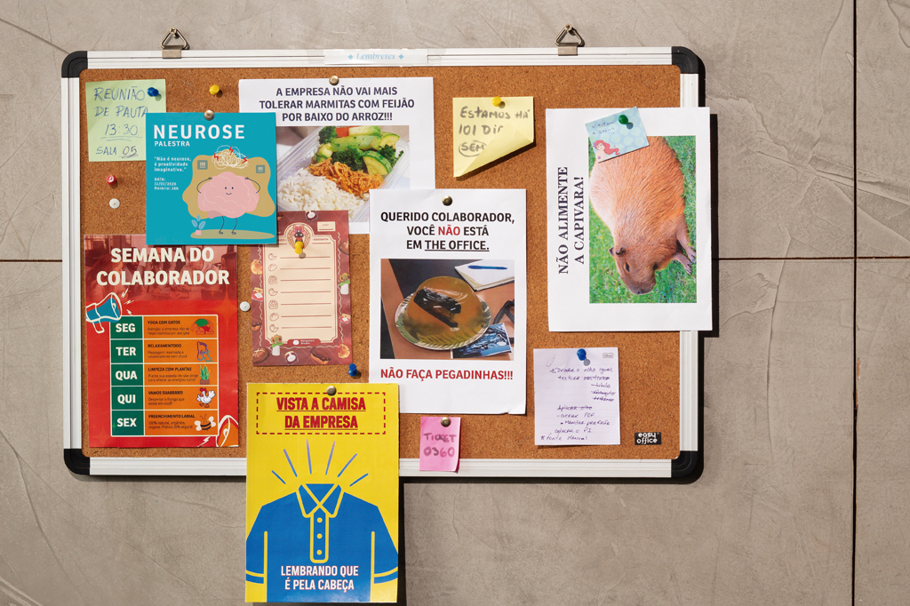 Imagem de uma parede, revestida de azulejos, com um painel feito de cortiça e diversos cartazes sobre ele.