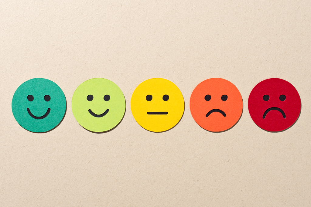 Imagem, em fundo bege escuro, de cinco emojis coloridos, feitos de papel, representando um estado de humor.