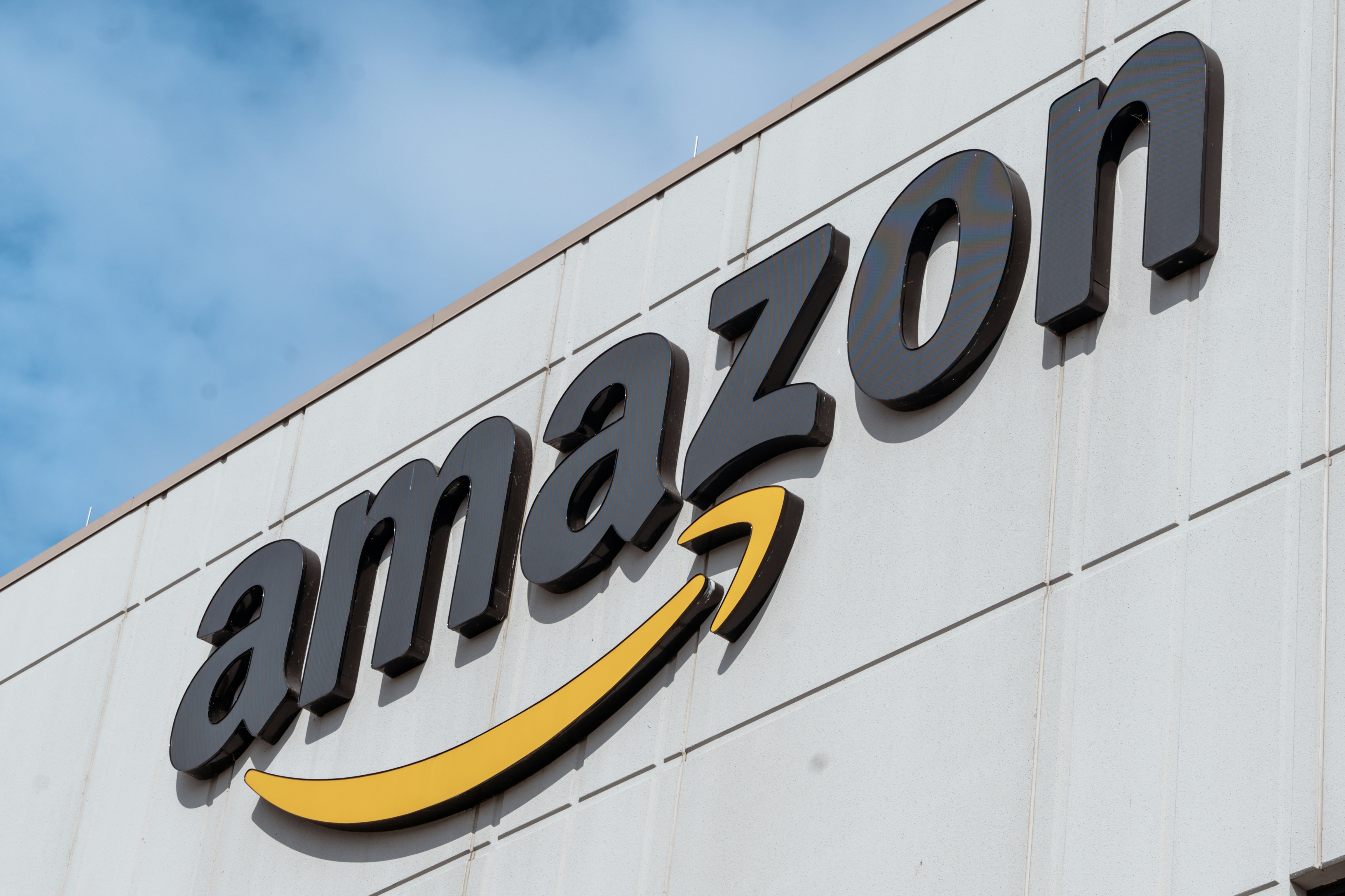 Letreiro da Amazon em letras pretas 3D com um sorriso amarelo e preto embaixo, fixado em uma parede branca de um prédio, sob um céu azul com nuvens esparsas