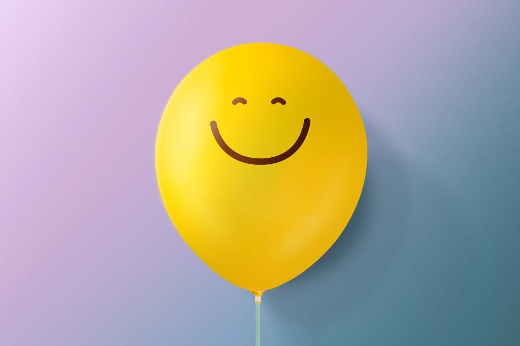 Balão amarelo com um rosto sorridente desenhado em marrom, flutuando contra um fundo gradiente de lilás a azul.