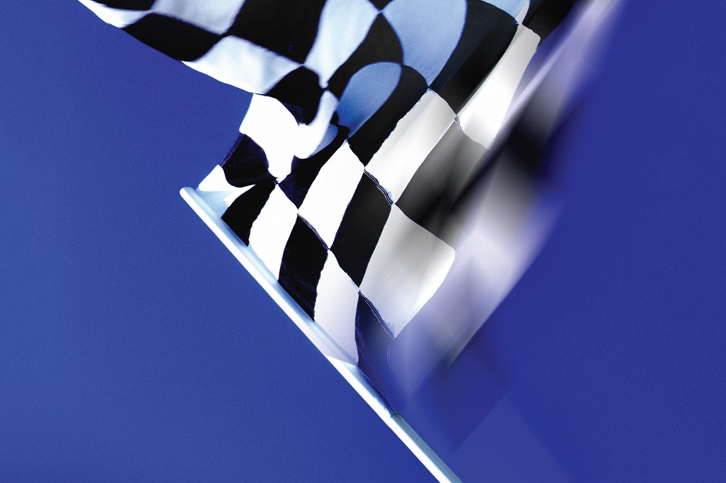 Bandeira quadriculada preta e branca, símbolo de vitória em corridas, tremulando rapidamente contra um céu azul vibrante, com efeito de movimento.